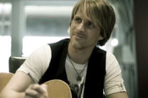 Jacob Moon sits and holds his guitar as writes at desk.